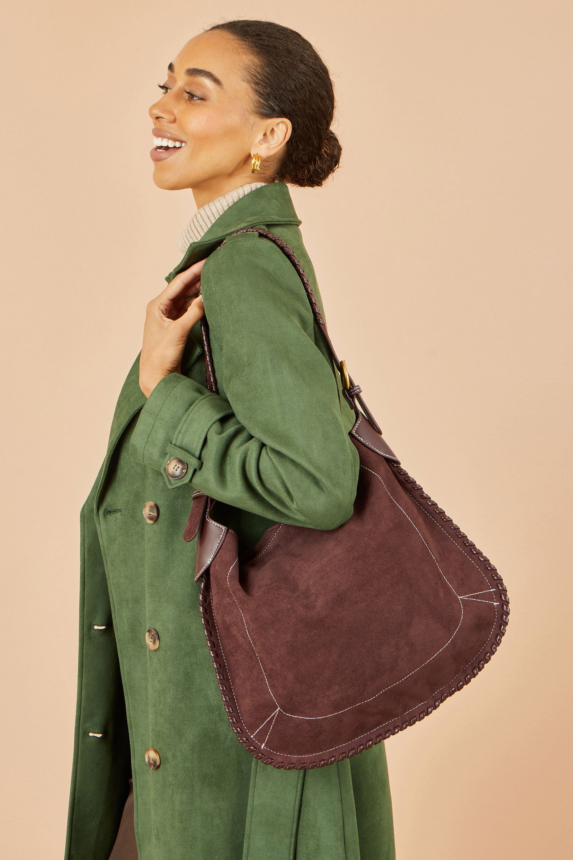 Woman in a green coat holding a brown leather bag against a beige background