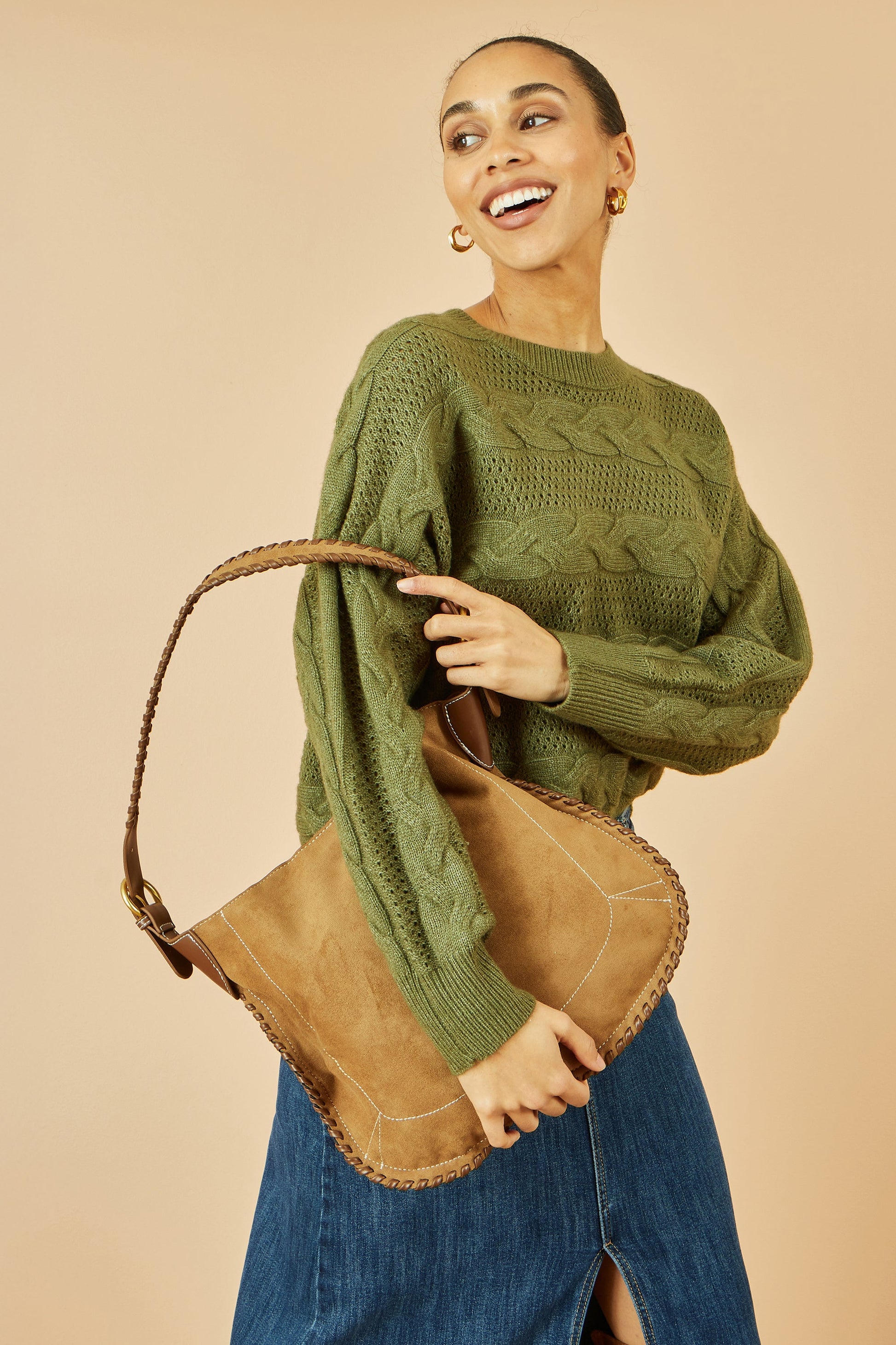 Woman wearing a green sweater holding a brown leather bag against a beige background
