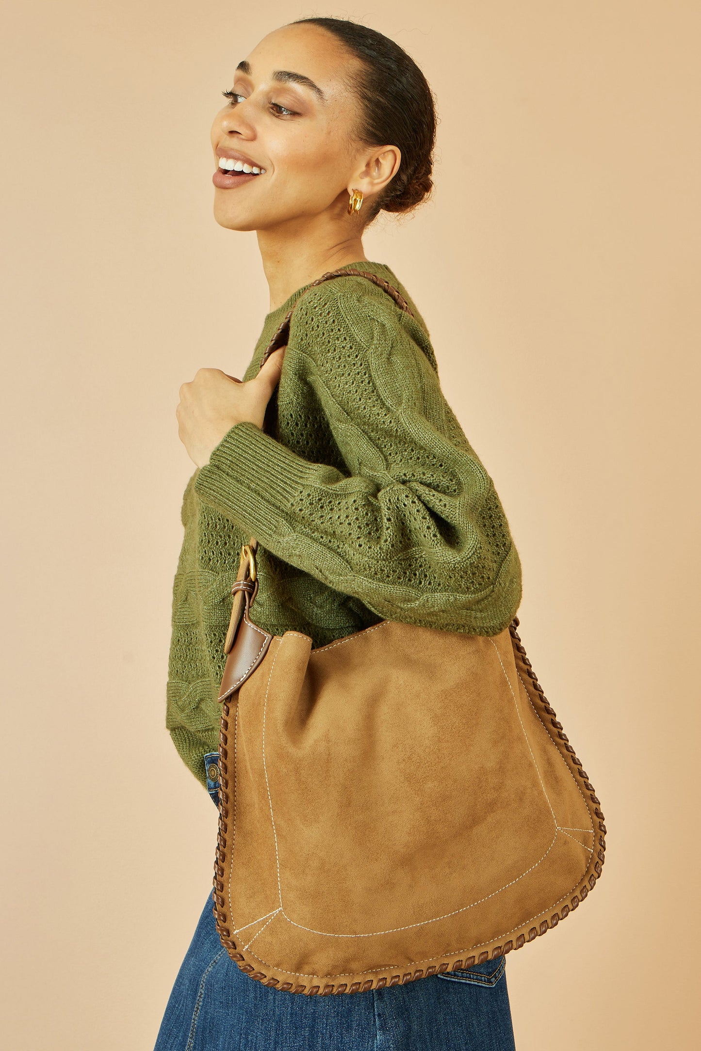 Woman wearing a green sweater and carrying a brown leather bag against a beige background