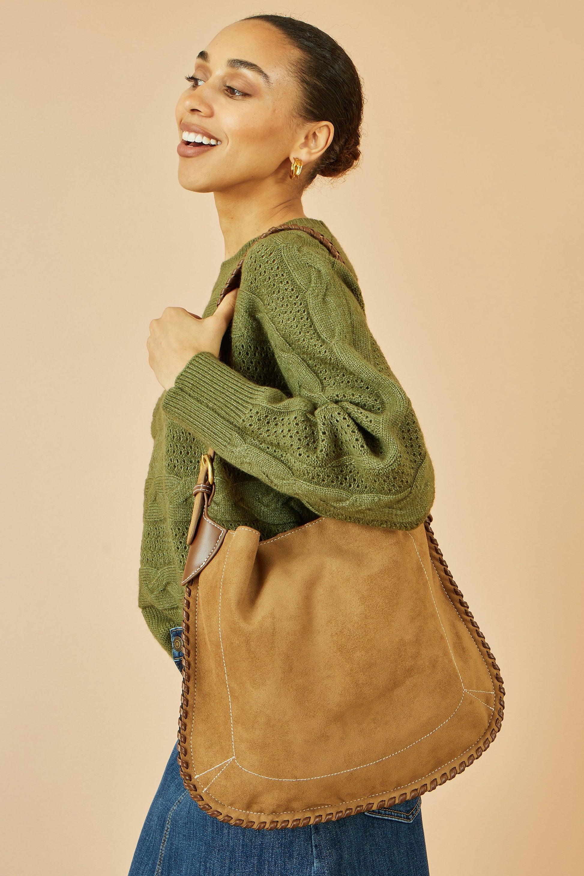 Woman wearing a green sweater and carrying a brown leather bag against a beige background