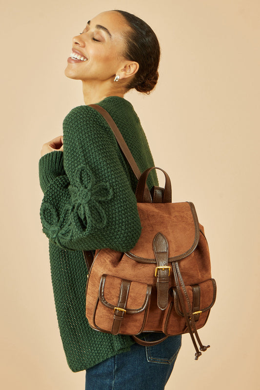 Woman wearing a green sweater and carrying a brown backpack against a beige background