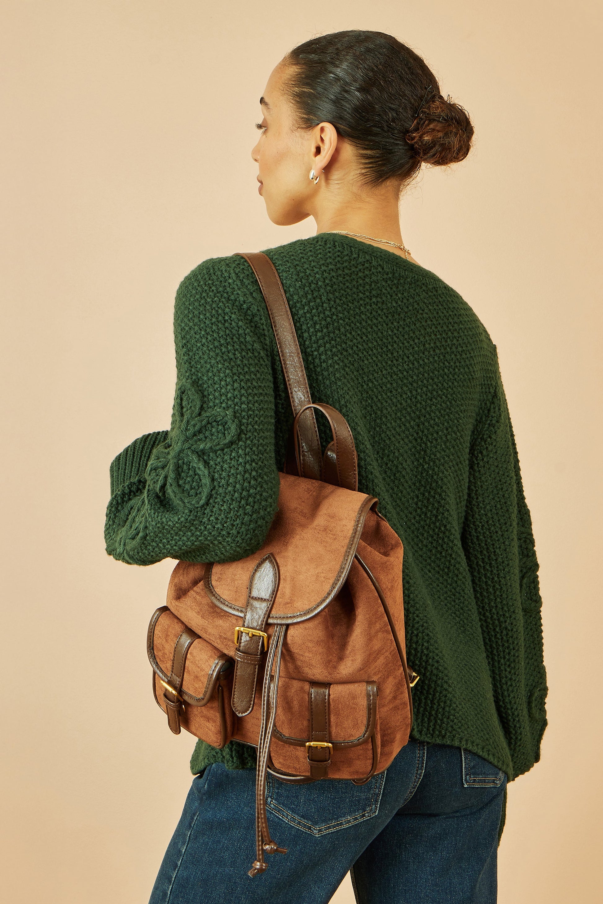 Woman wearing a green sweater and brown backpack on a beige background
