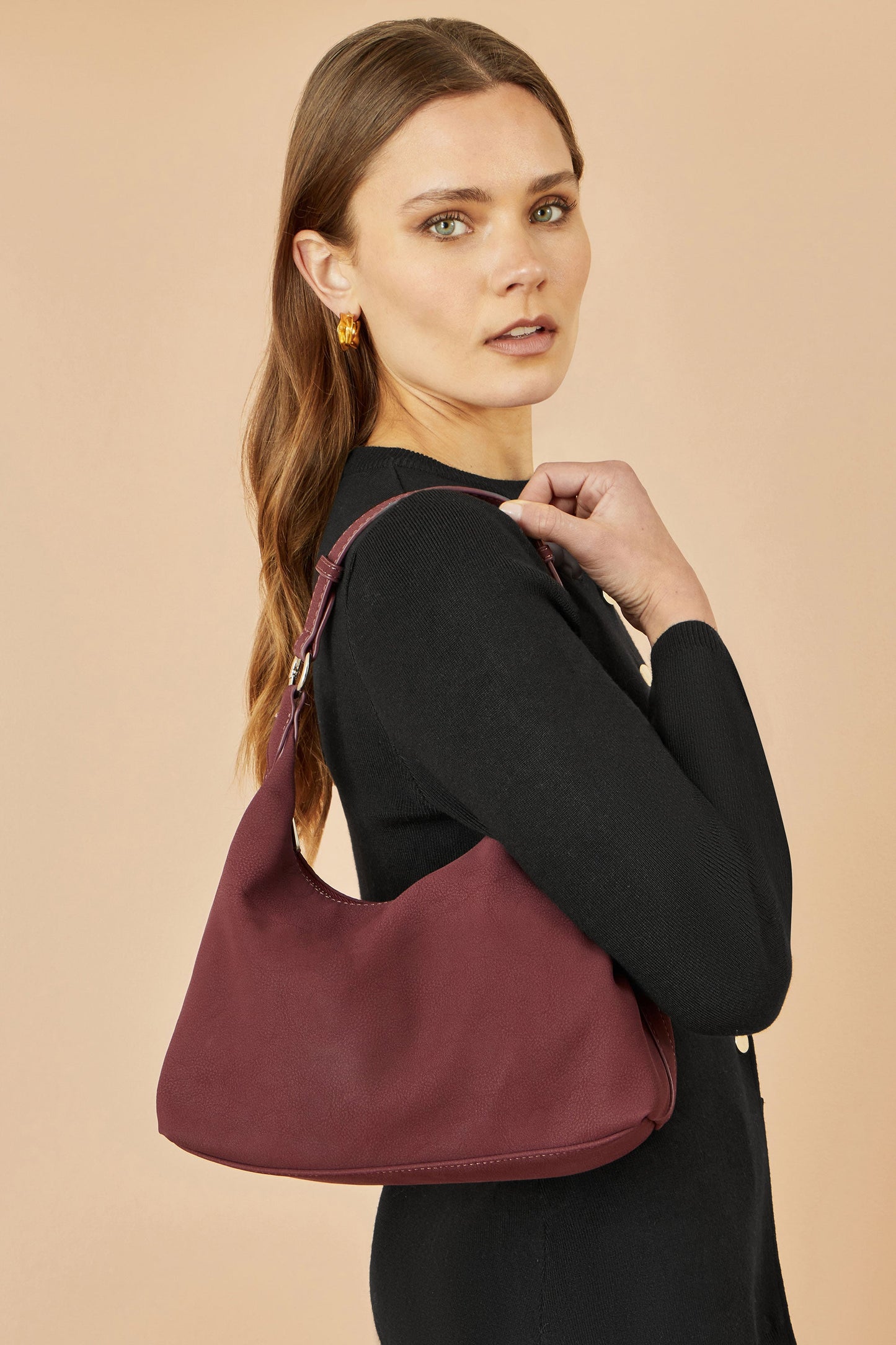 Woman carrying a burgundy handbag against a beige background