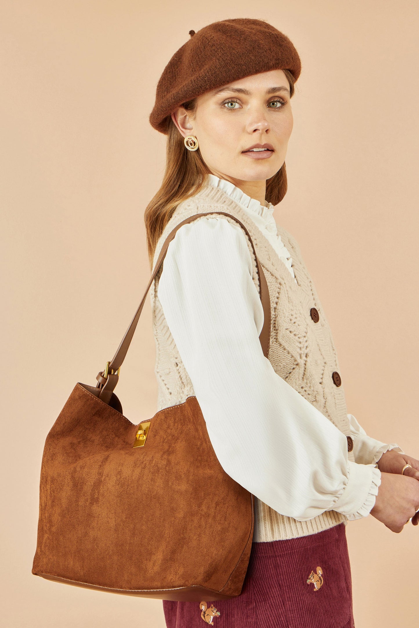 Woman wearing a brown beret and holding a brown handbag against a beige background