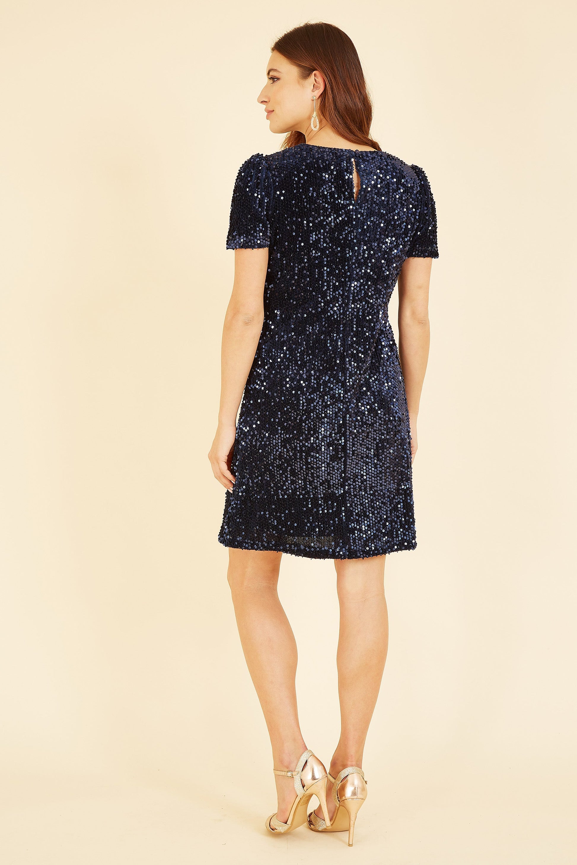 Woman wearing a navy sequin dress on a beige background