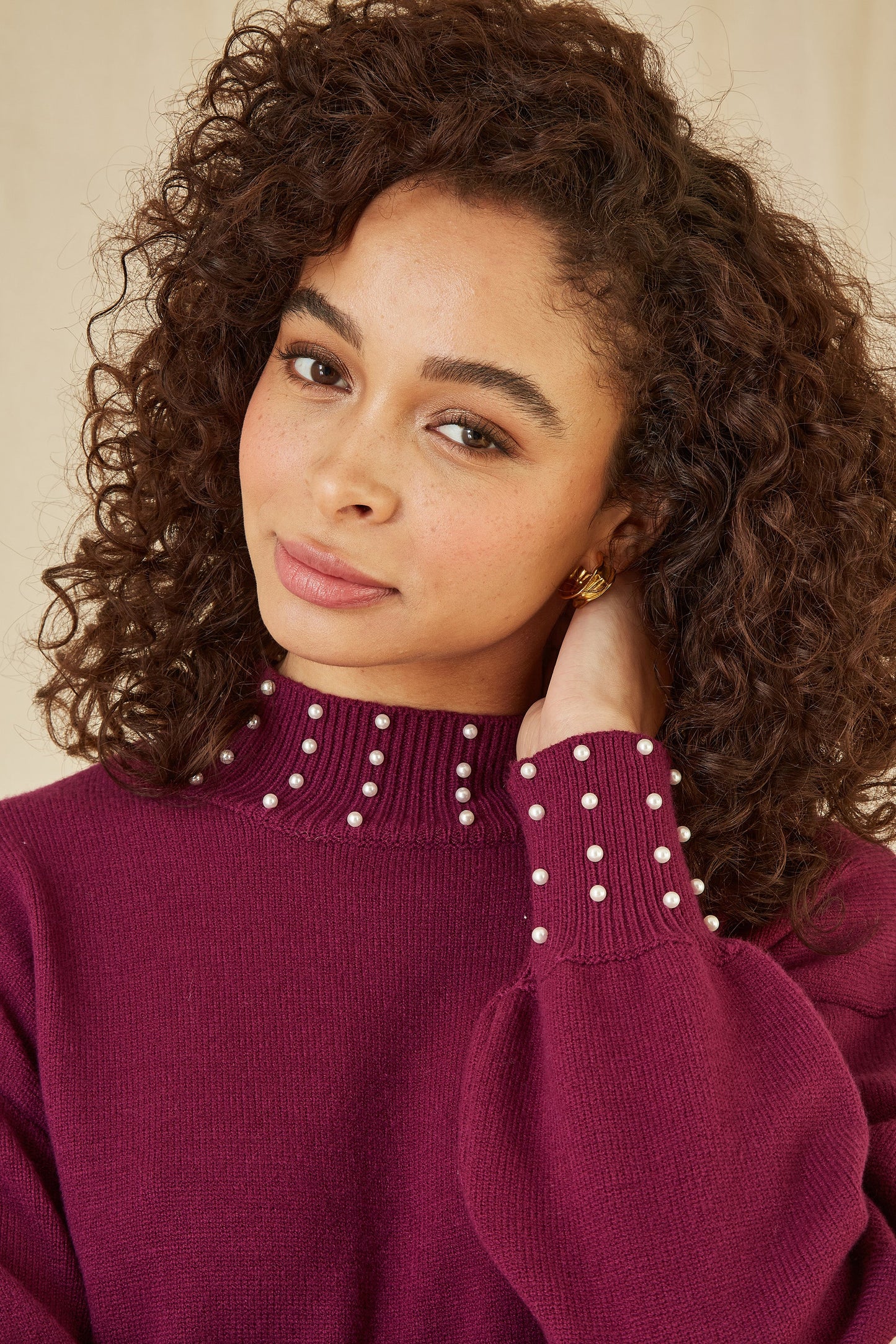 Woman wearing a maroon sweater with pearl details against a neutral background
