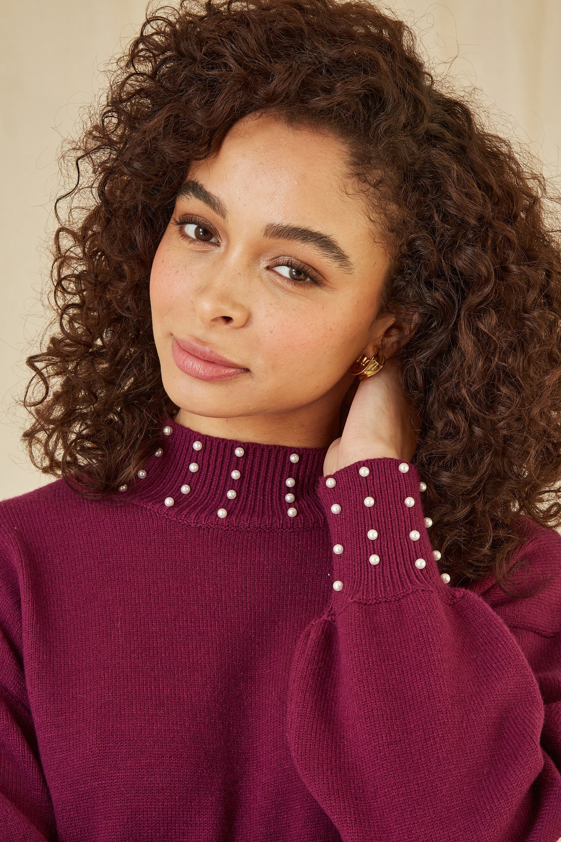 Woman wearing a maroon sweater with pearl details against a neutral background
