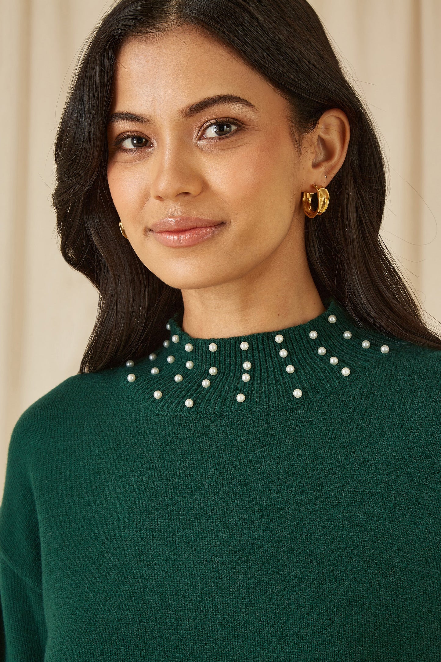 Woman wearing a green sweater with a pearl neckline against a beige background