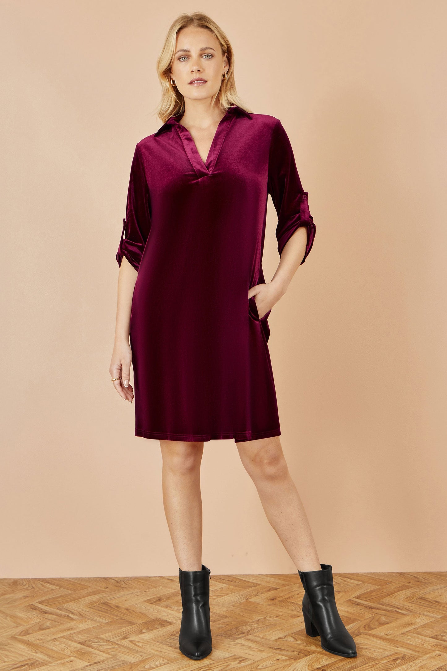Woman wearing a burgundy dress with black boots on a beige background