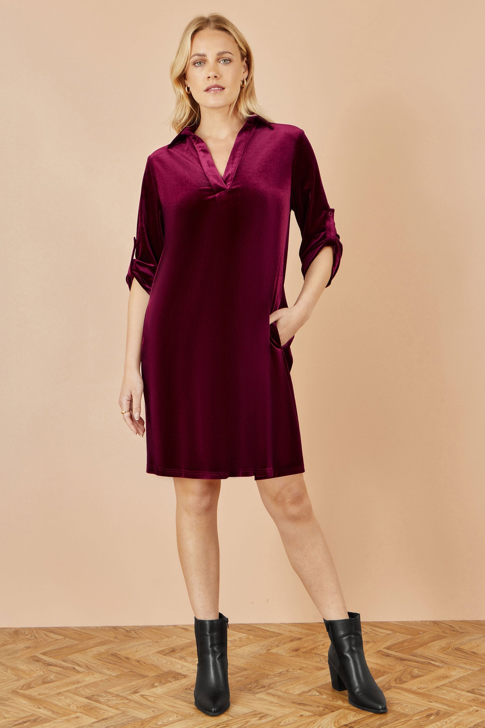 Woman wearing a burgundy dress with black boots on a beige background