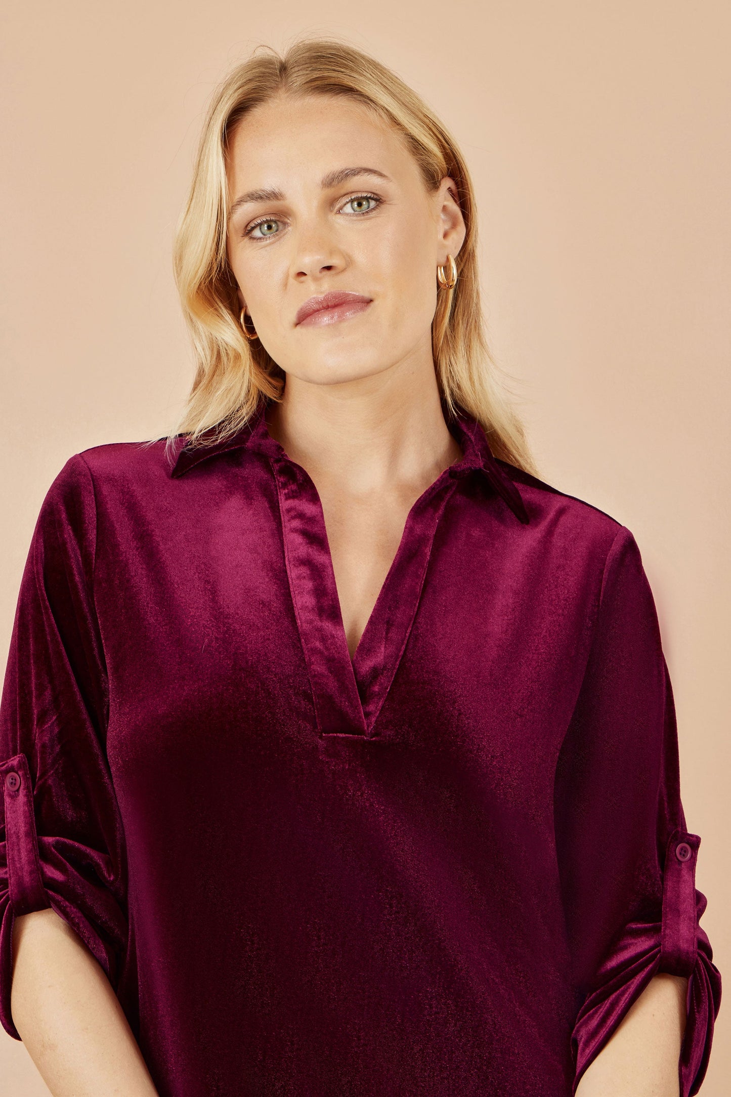Woman wearing a burgundy velvet shirt against a beige background