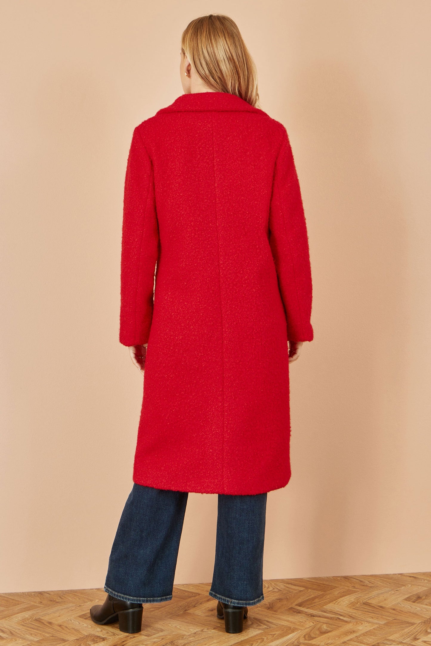 Person wearing a red coat standing against a beige wall.