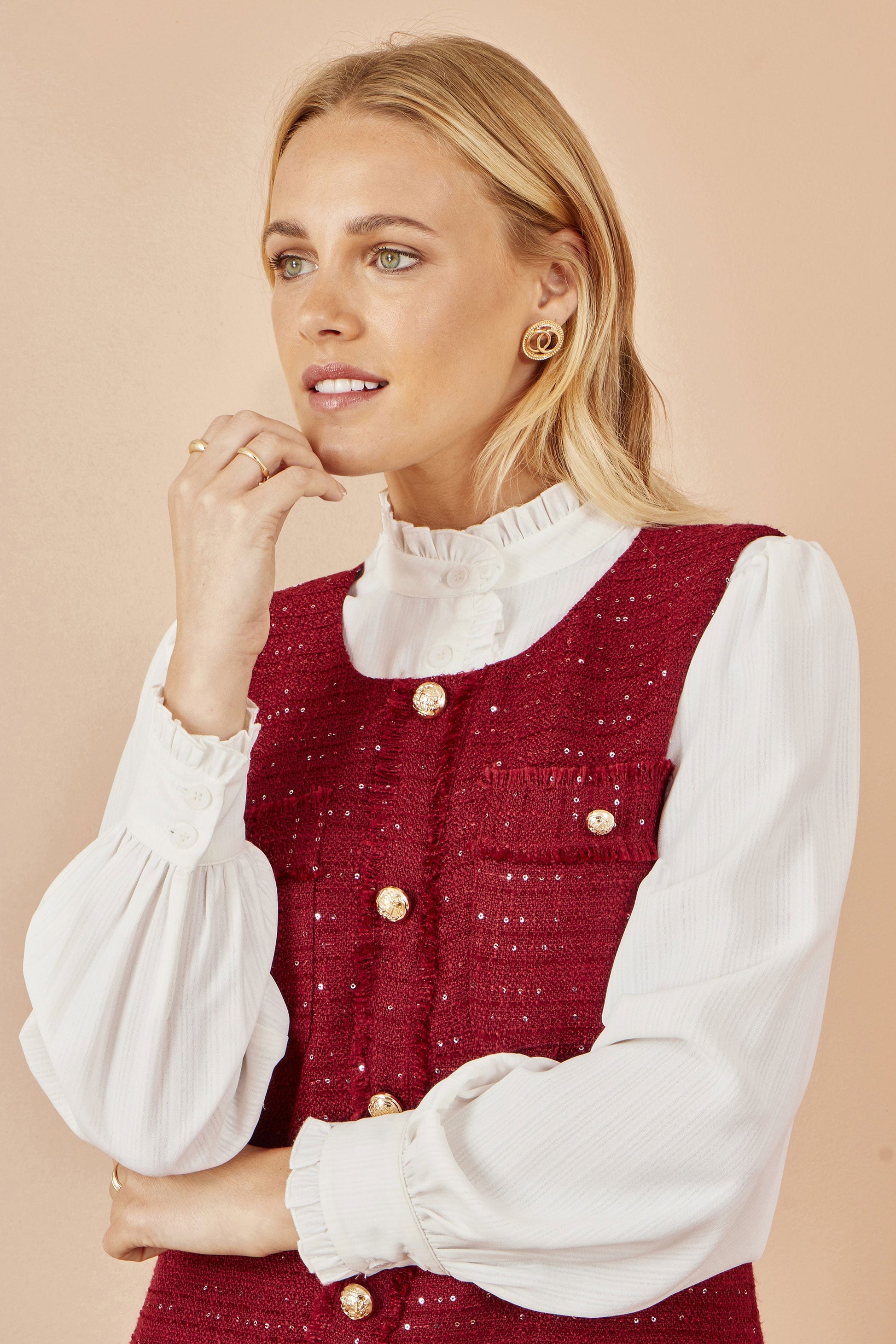 Woman wearing a red vest over a white blouse with a beige background