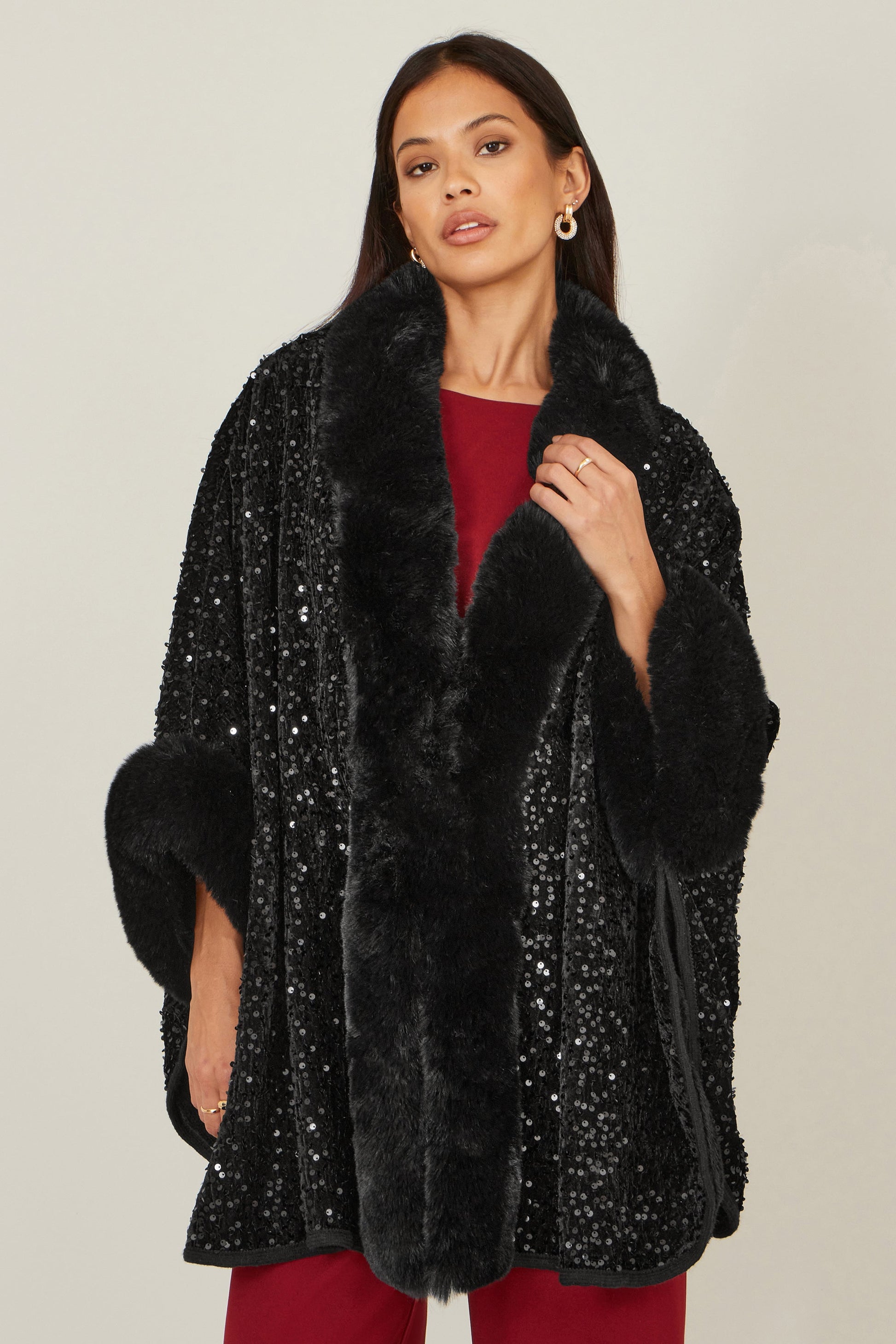Woman wearing a black sequin coat with fur trim on a plain background