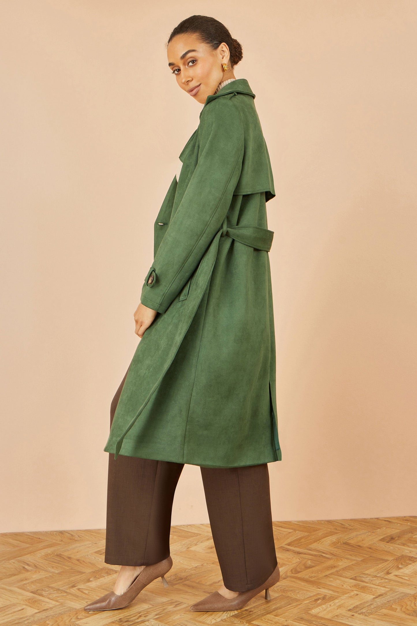Woman wearing a green trench coat on a beige background