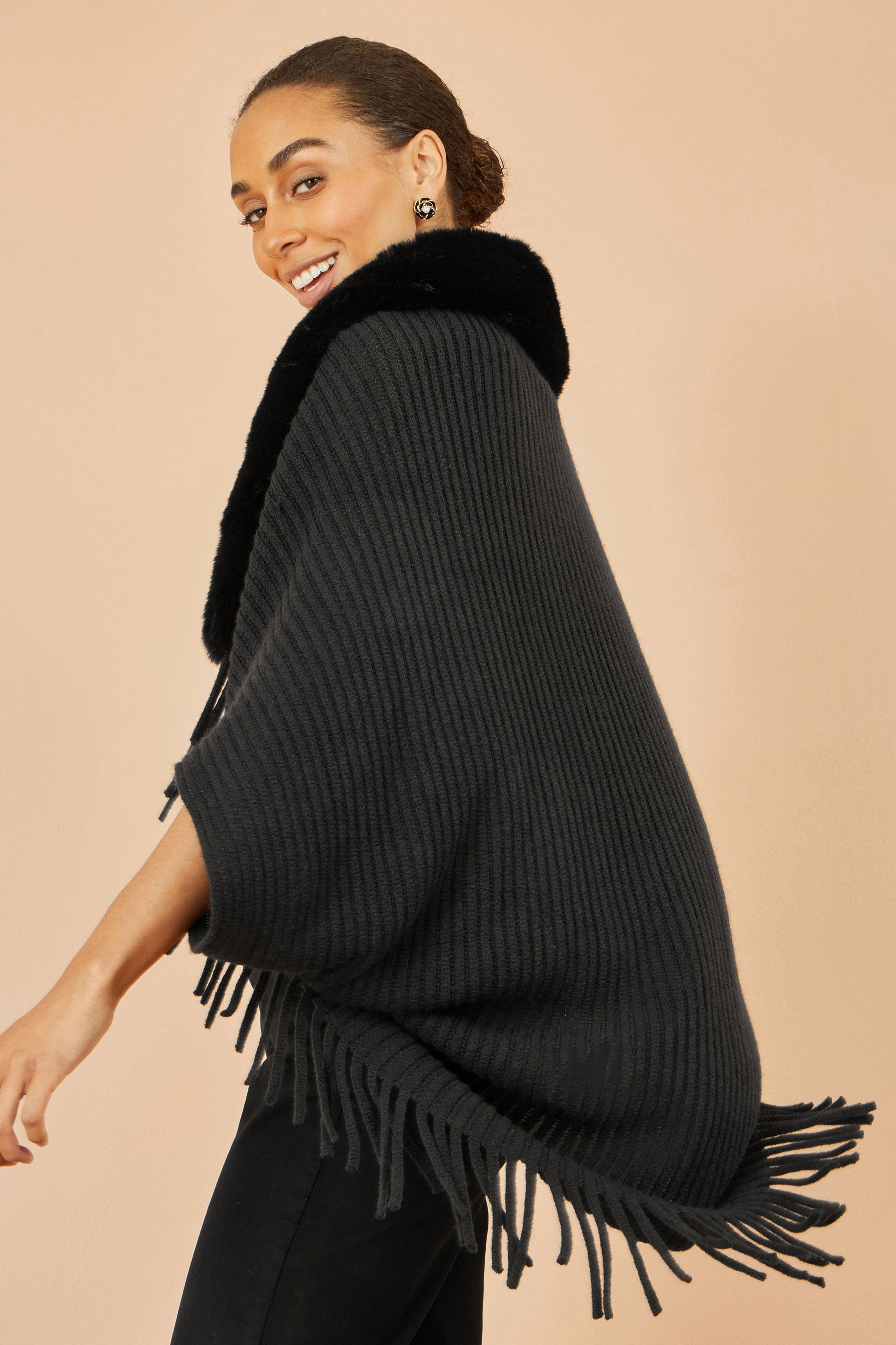 Woman wearing a black poncho with fringe on a beige background