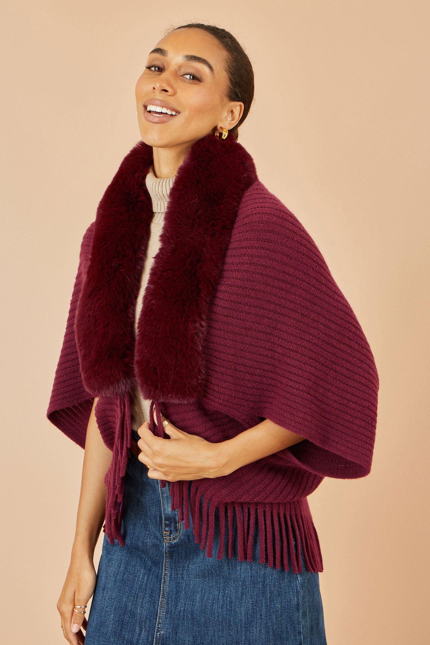 Woman wearing a burgundy poncho with fur trim against a beige background