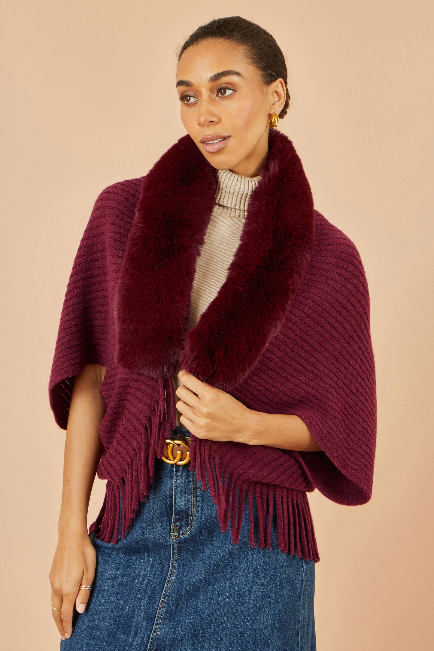 Woman wearing a burgundy poncho with fringe on a beige background