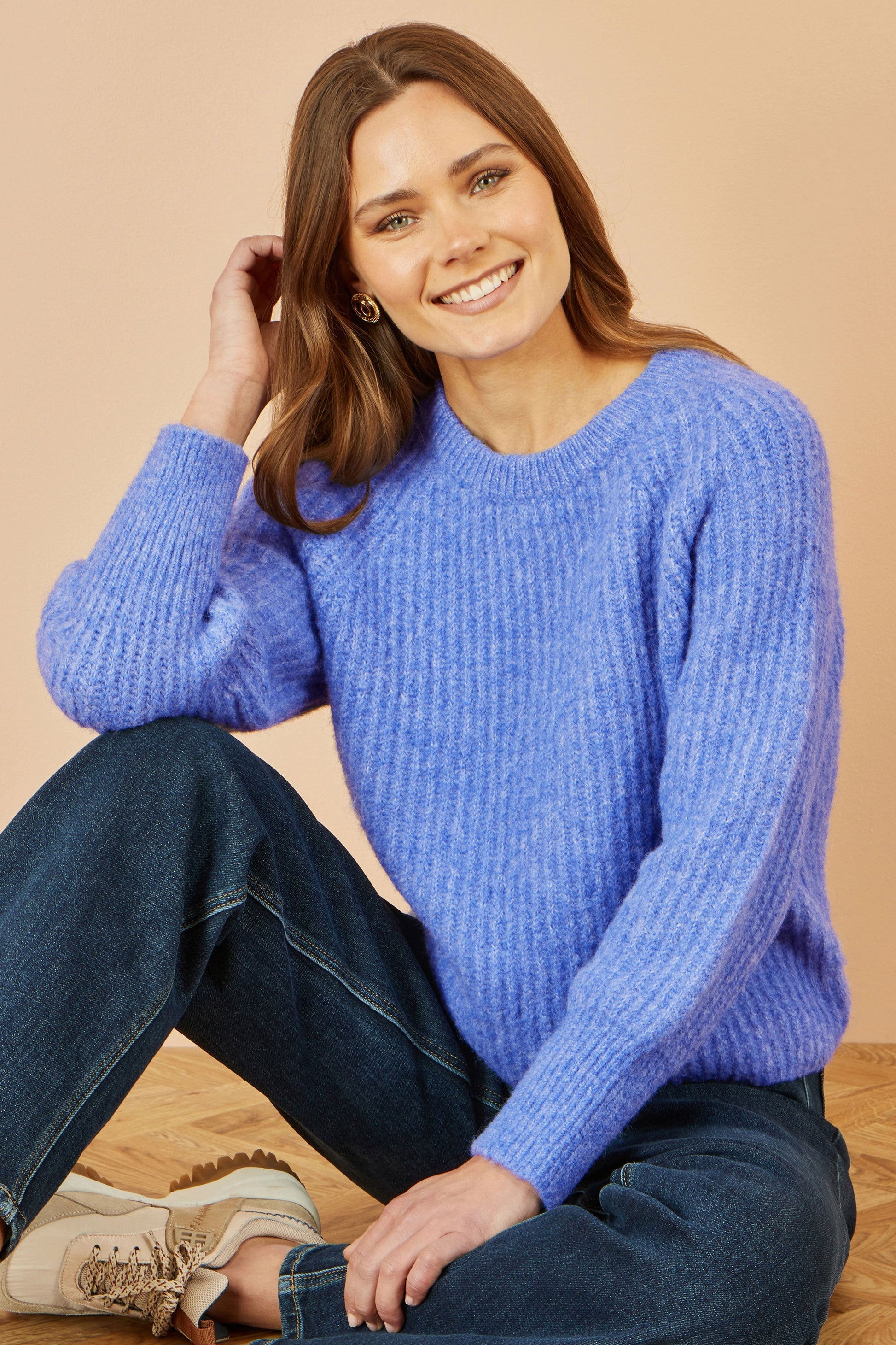 Woman wearing a blue sweater sitting on the floor against a beige background