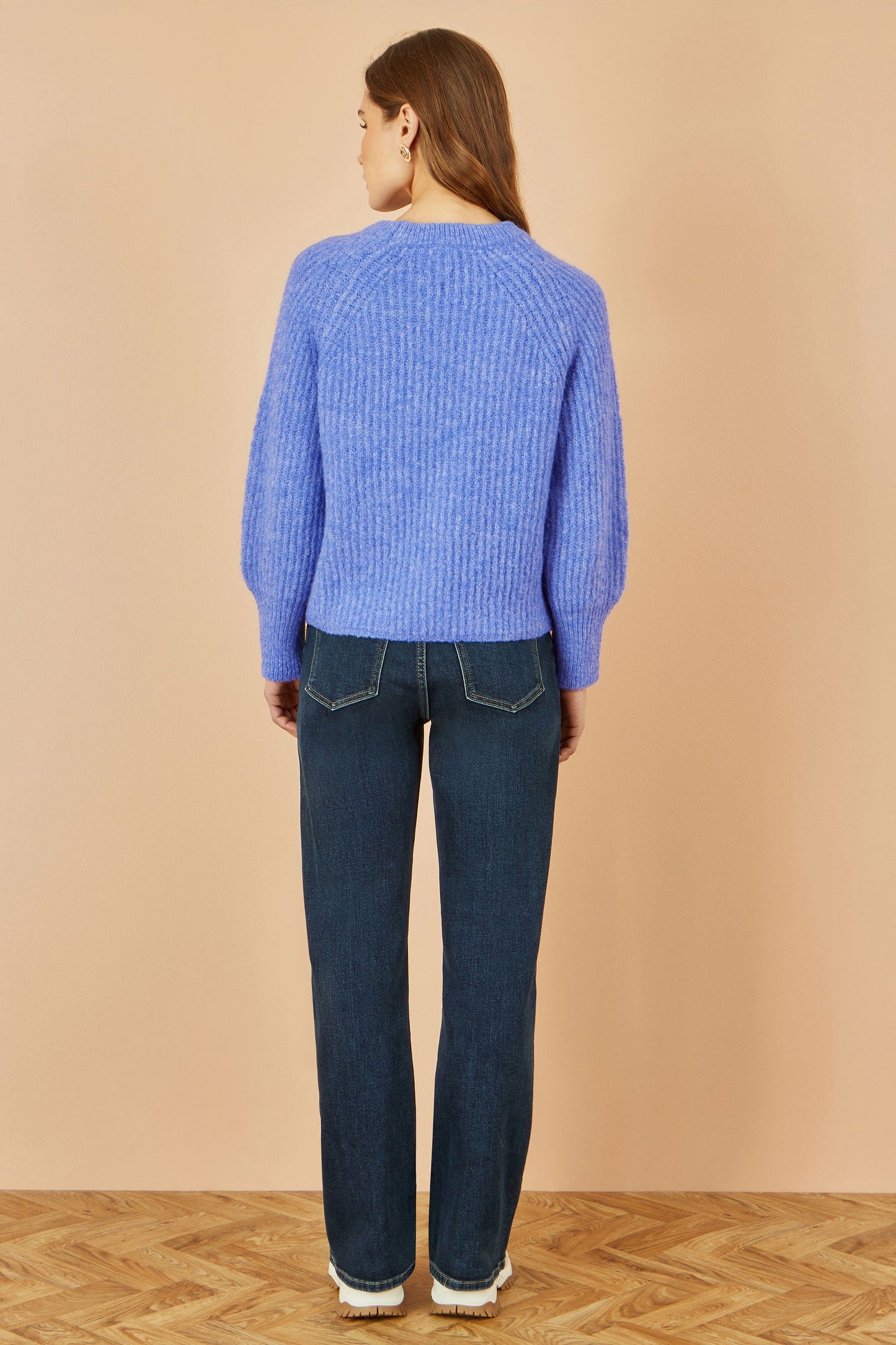 Person wearing a blue sweater and dark jeans on a beige background