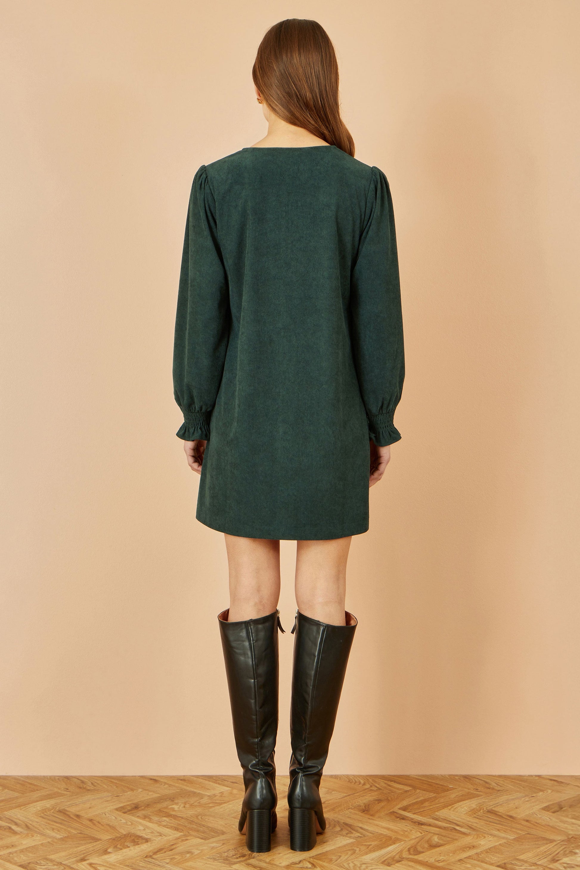 Woman wearing a green dress and black boots on a beige background