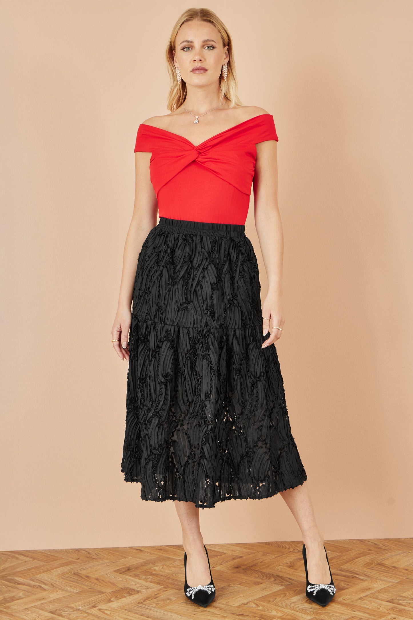 Woman wearing a red top and black lace skirt against a beige background