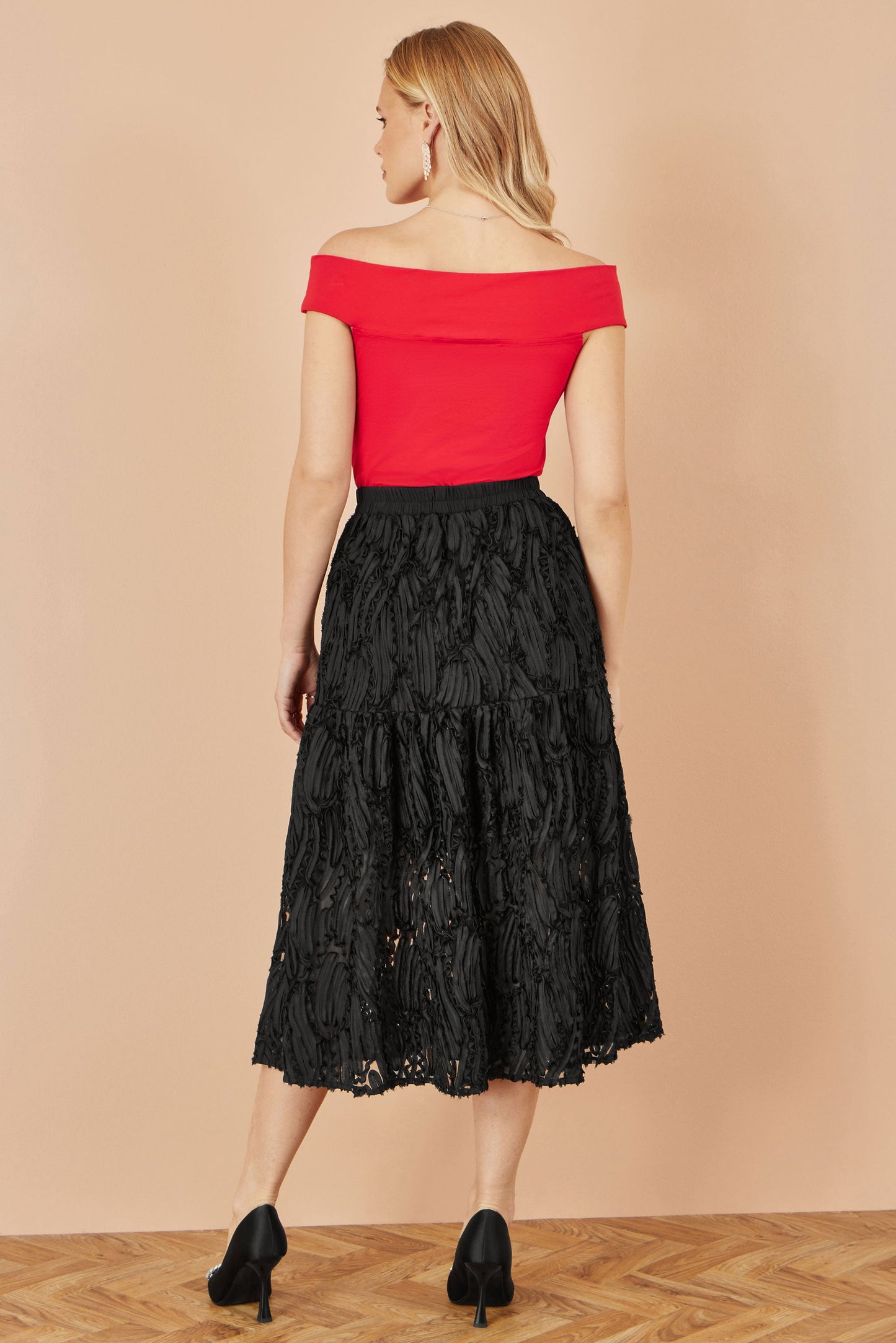 Woman wearing a red top and black lace skirt on a beige background