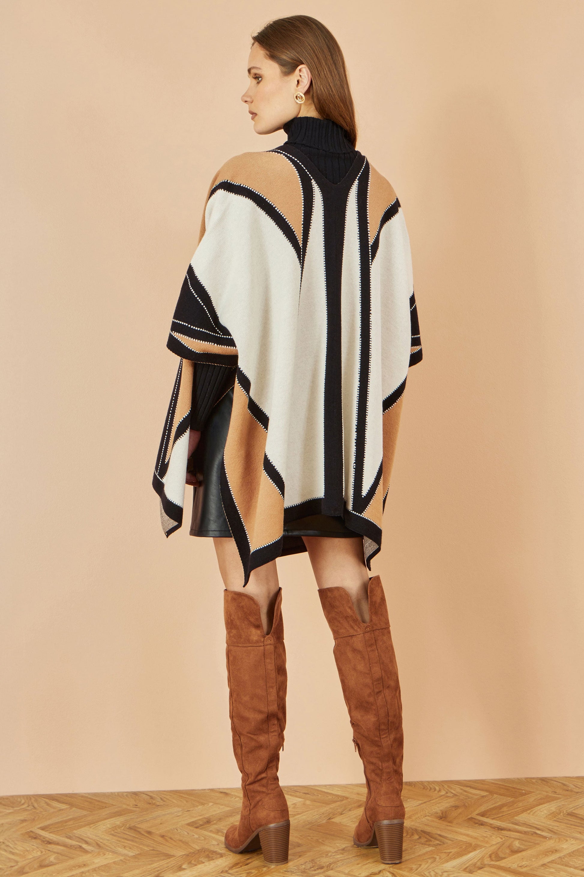 Woman wearing a black and white striped poncho with brown knee-high boots on a beige background