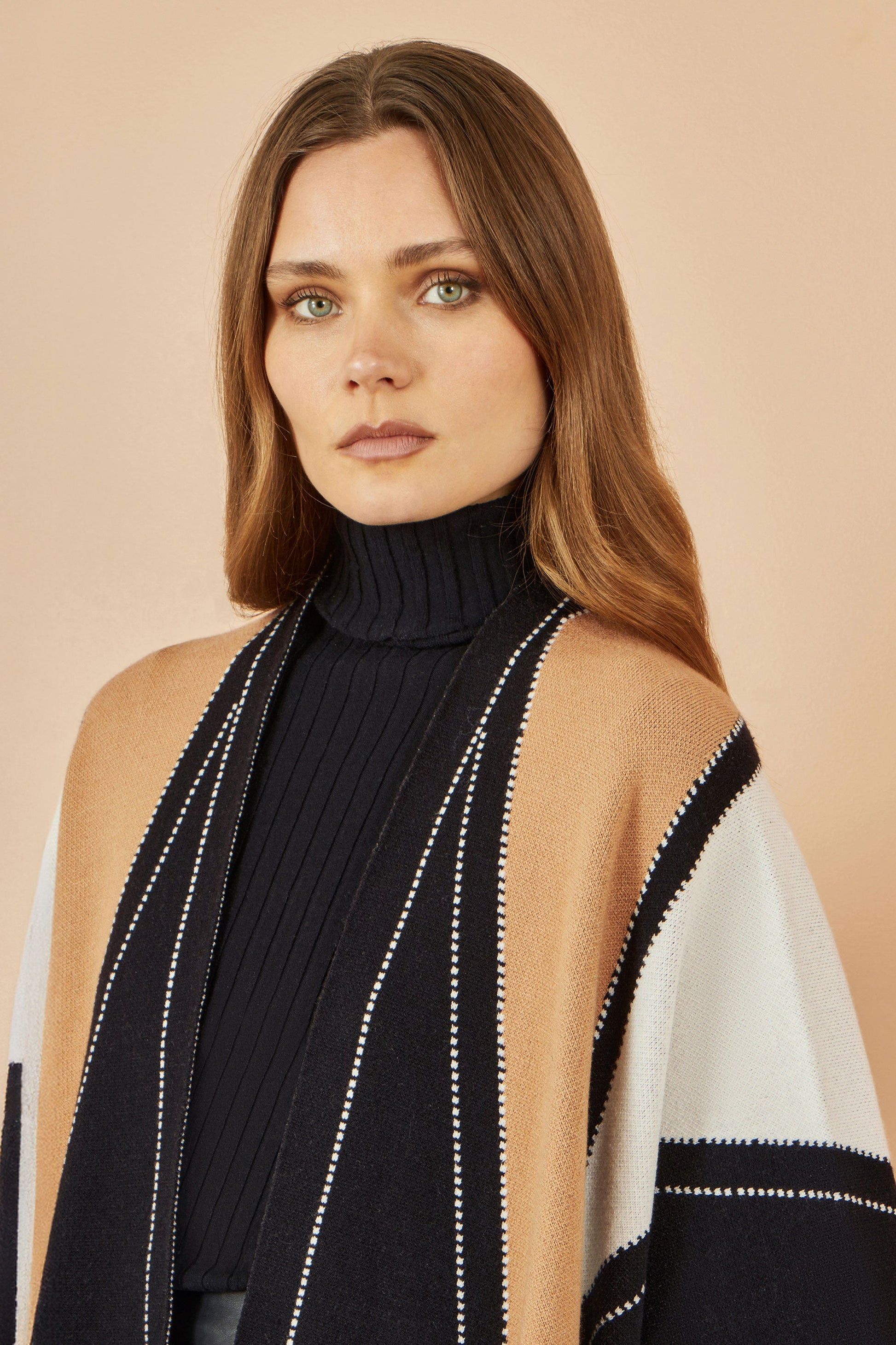 Woman wearing a black turtleneck and a beige and black patterned shawl on a beige background