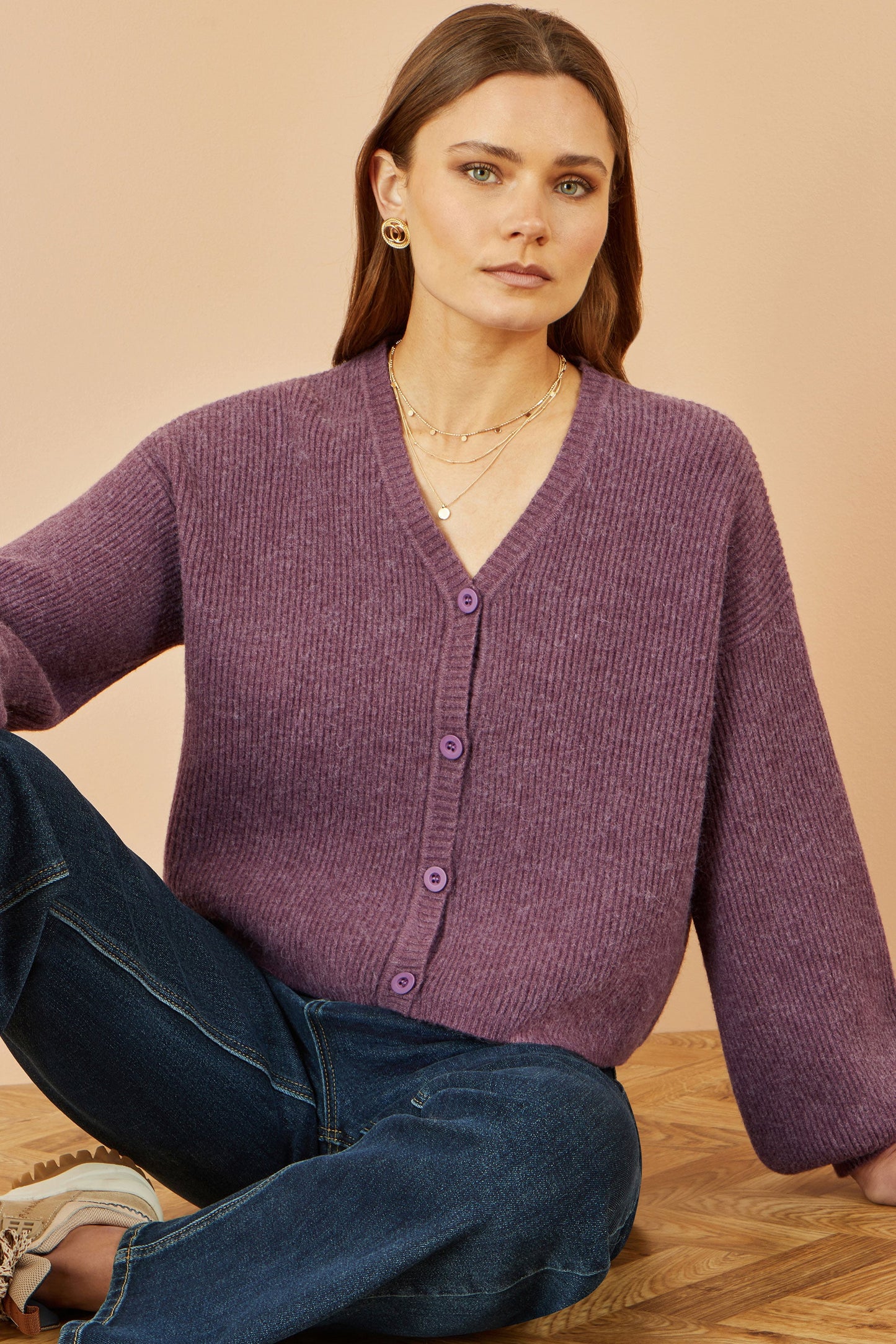 Woman wearing a purple cardigan sitting on a wooden floor with a beige background