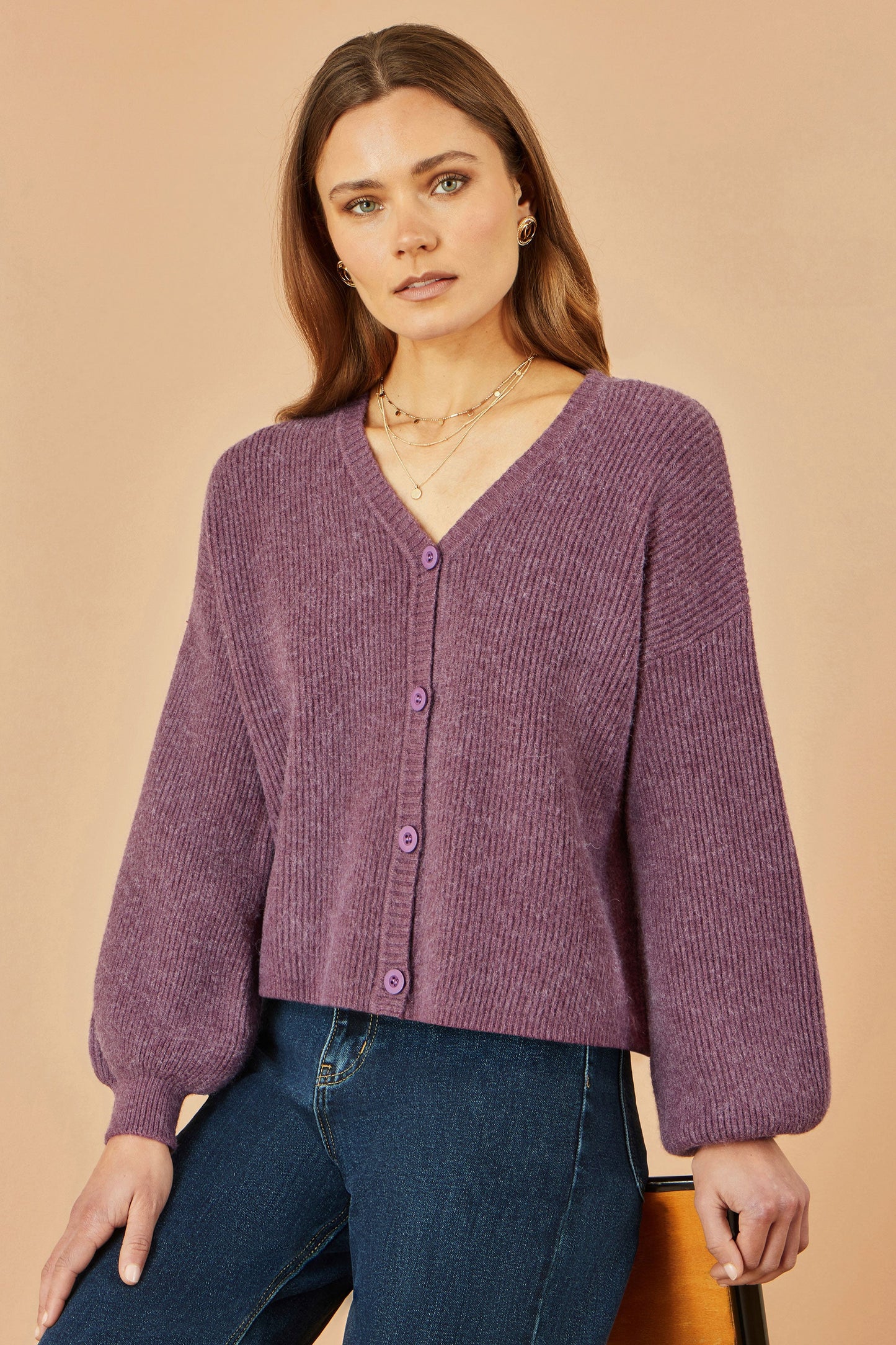 Woman wearing a purple cardigan and blue jeans against a beige background