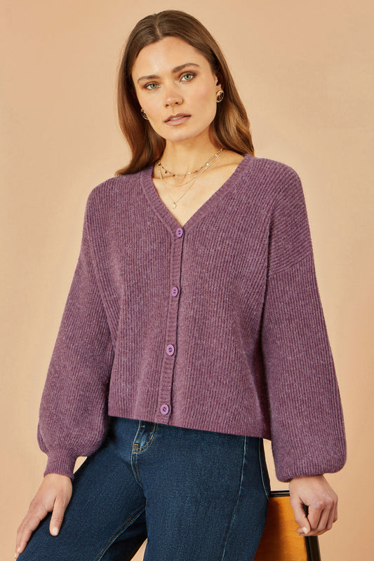 Woman wearing a purple cardigan and blue jeans against a beige background