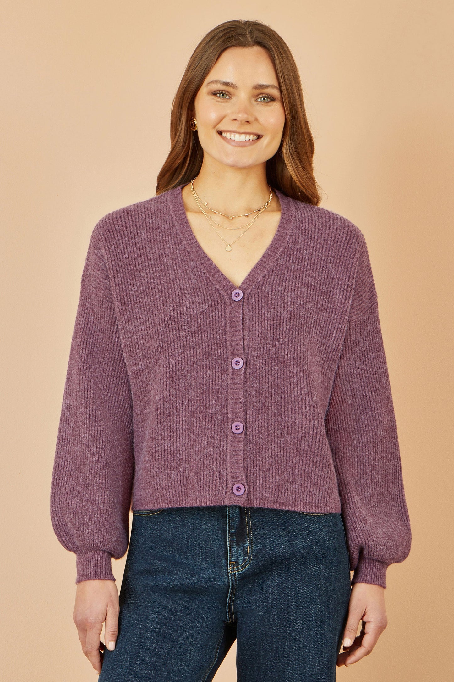 Woman wearing a purple cardigan and blue jeans on a beige background