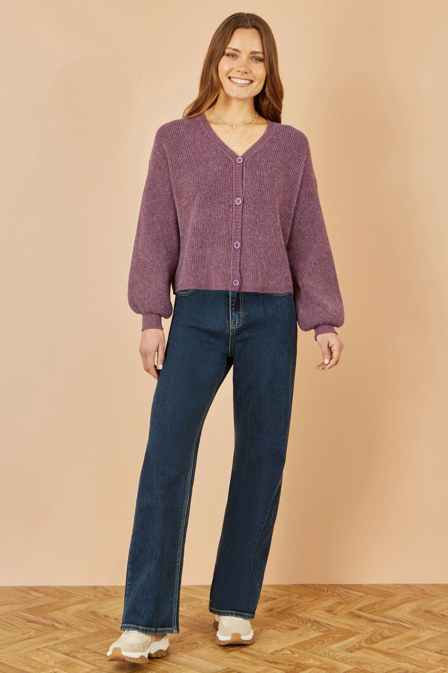 Woman wearing a purple cardigan and blue jeans against a beige background