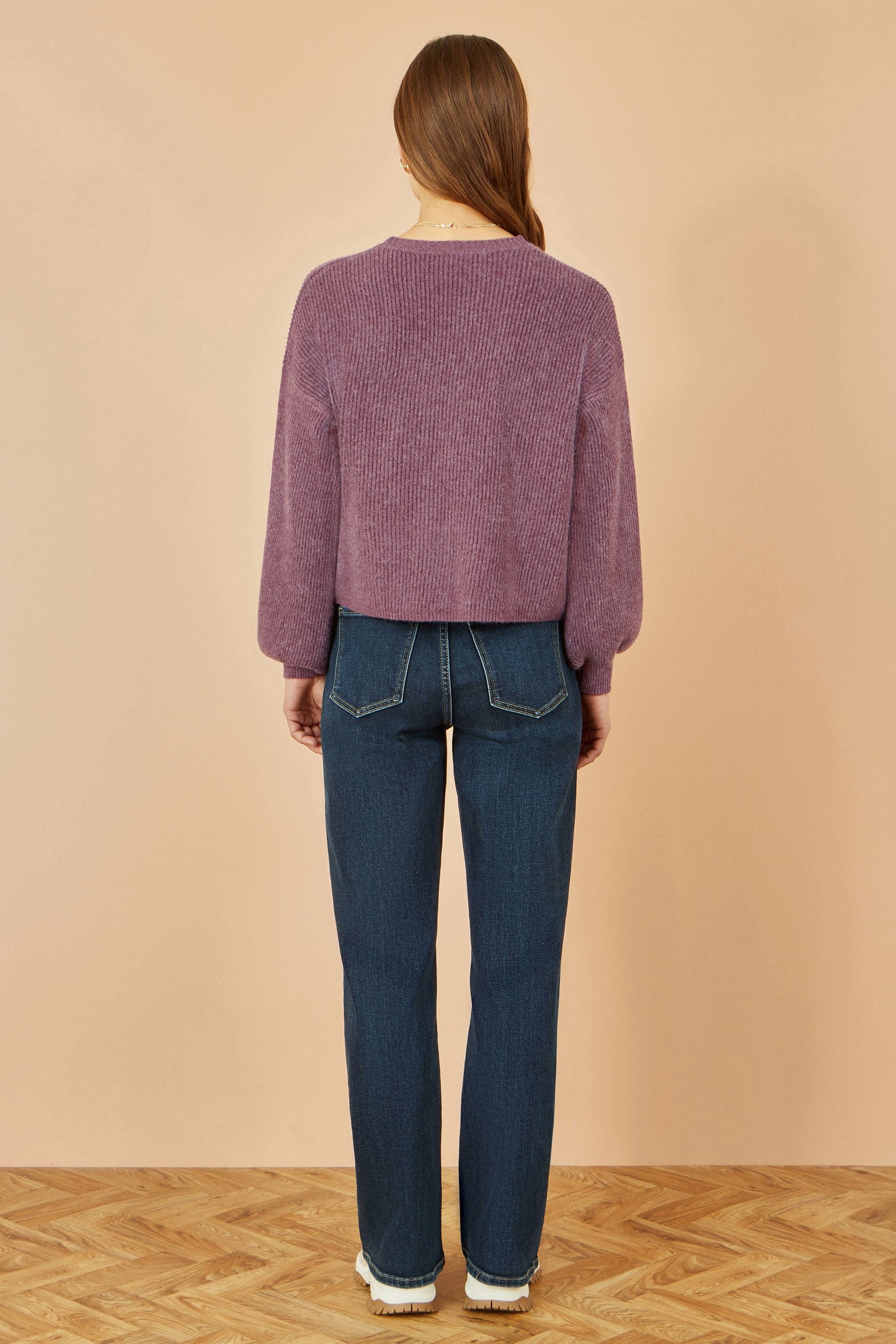 Person wearing a purple sweater and blue jeans against a beige background