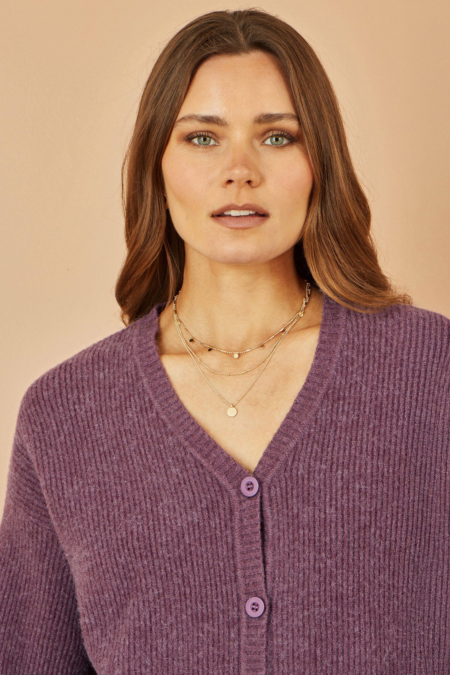 Woman wearing a purple cardigan with layered necklaces against a beige background