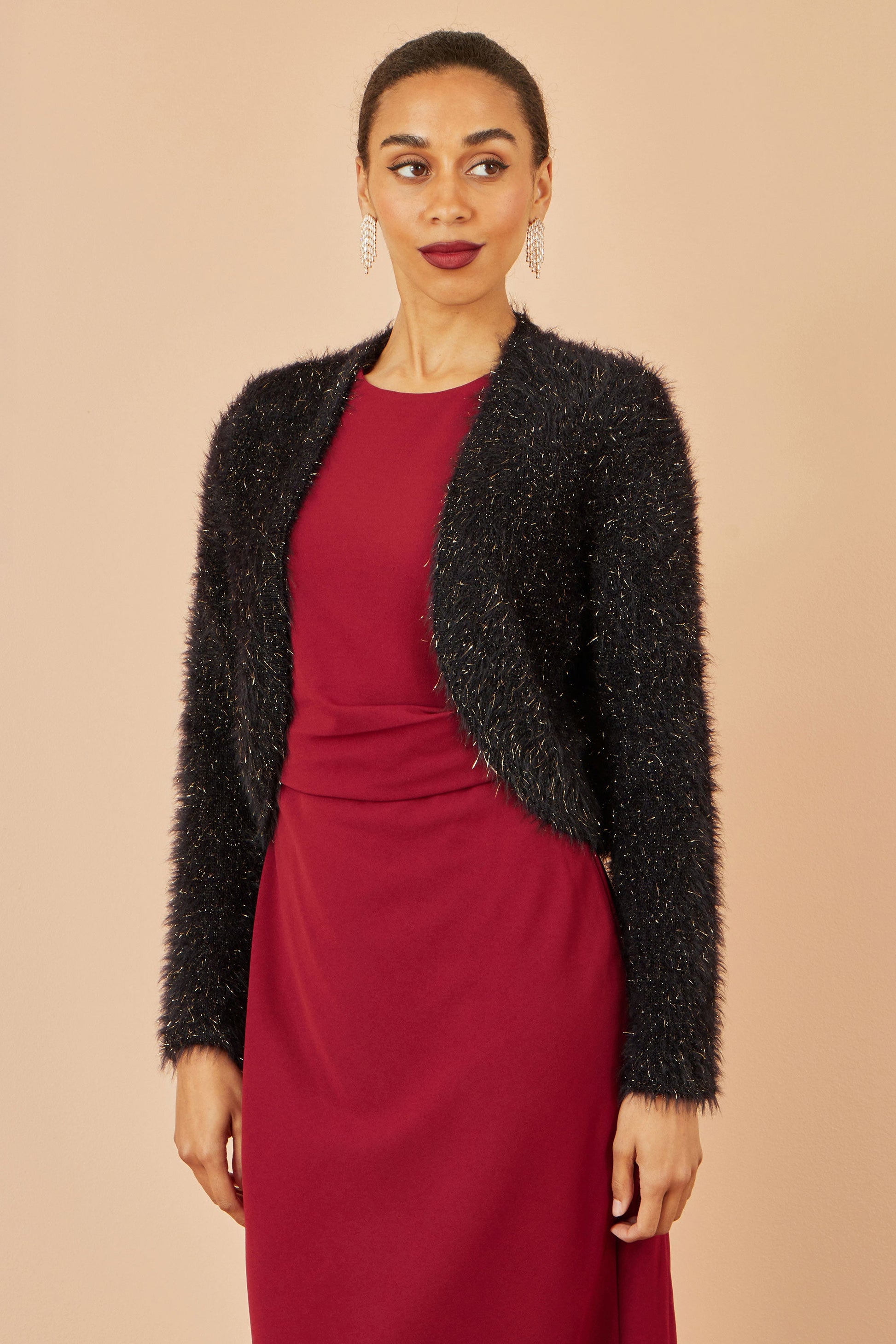 Woman wearing a black textured cardigan over a red dress on a beige background