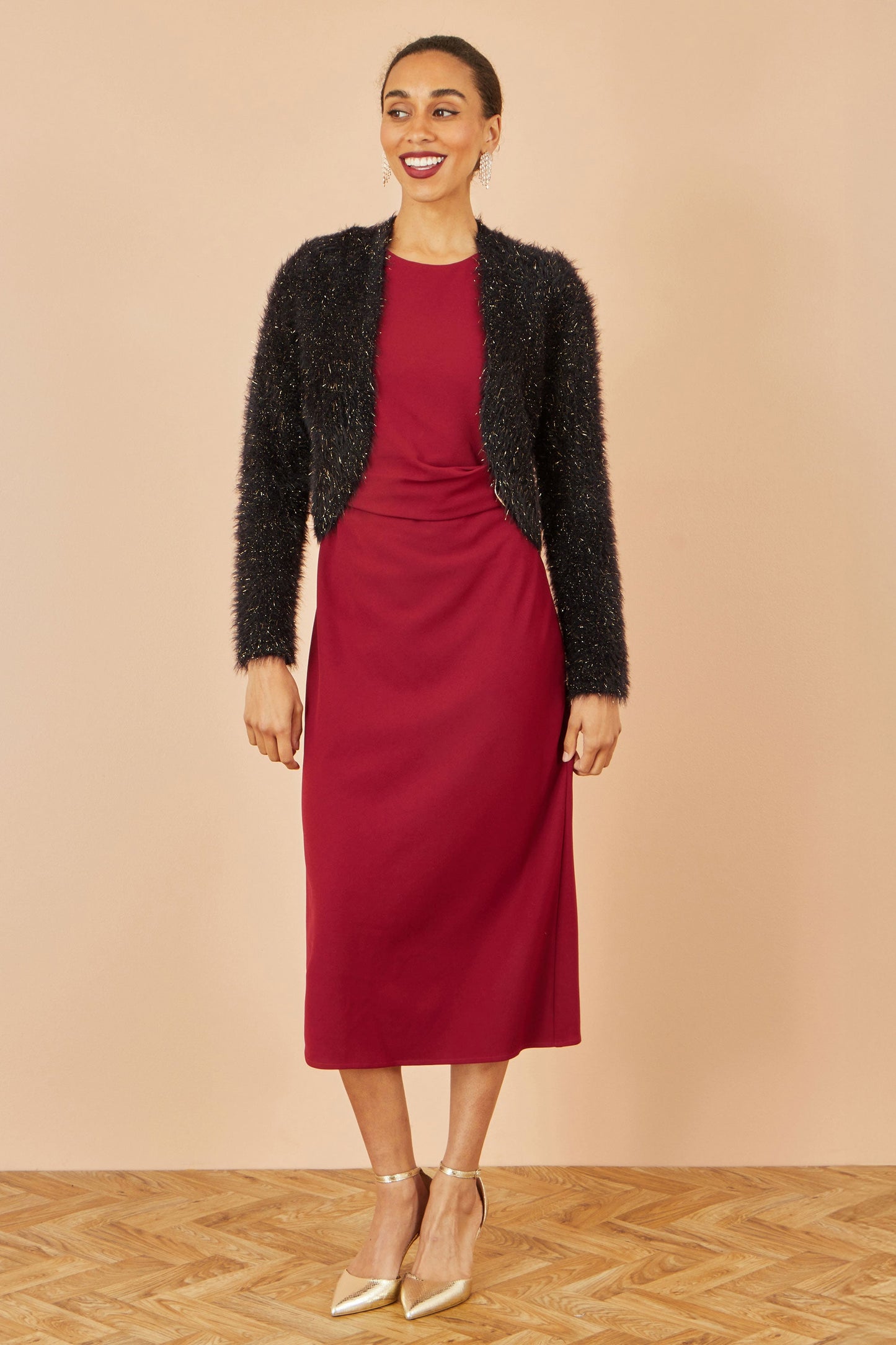 Woman wearing a red dress and black cardigan on a beige background
