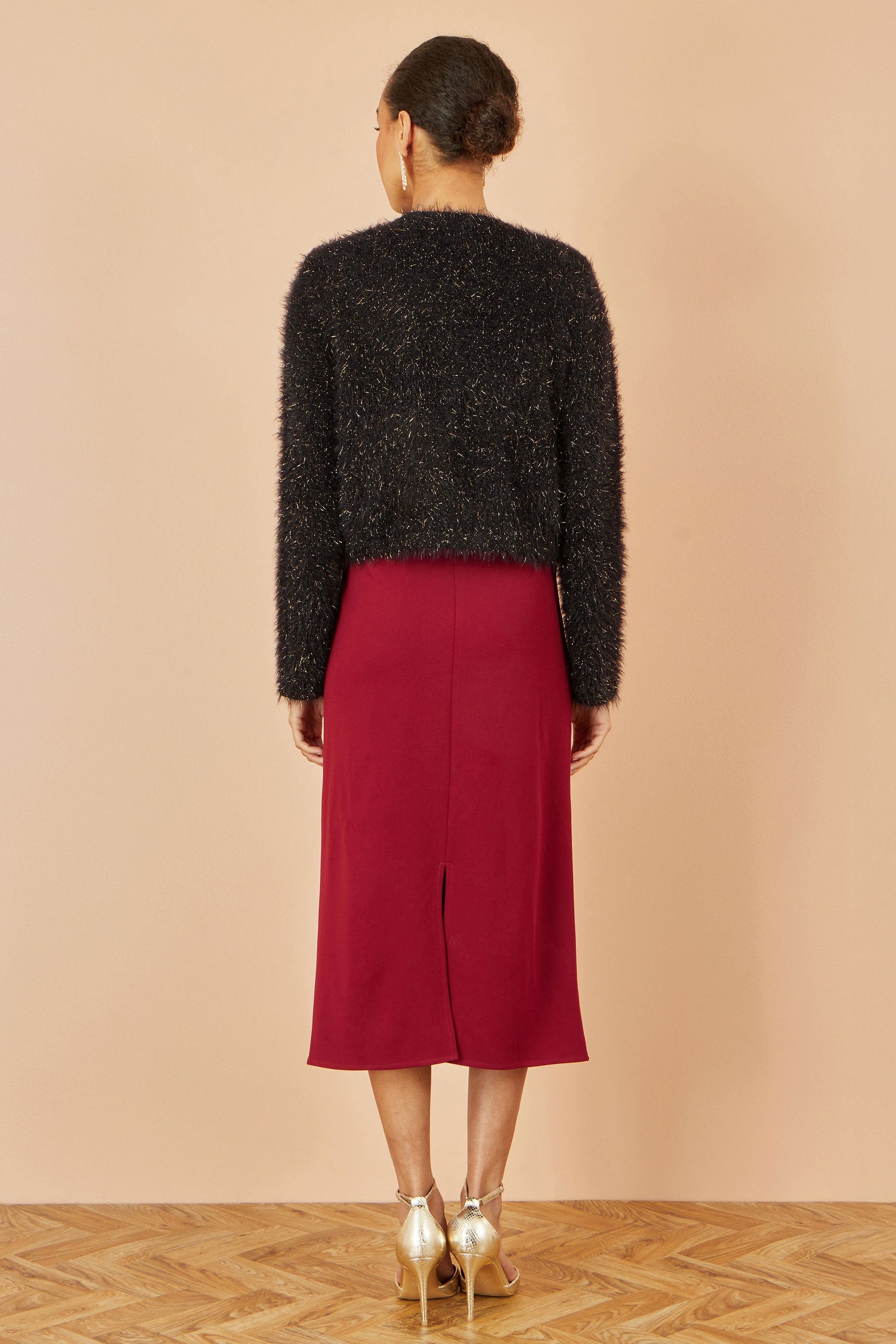 Person wearing a black textured sweater and red skirt on a beige background