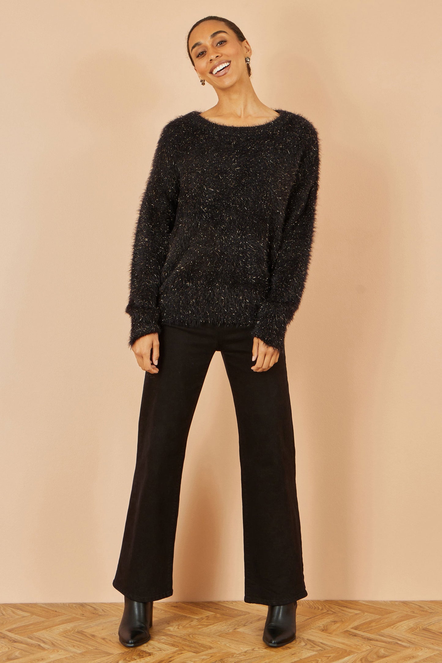 Person wearing a black textured sweater and black pants on a beige background