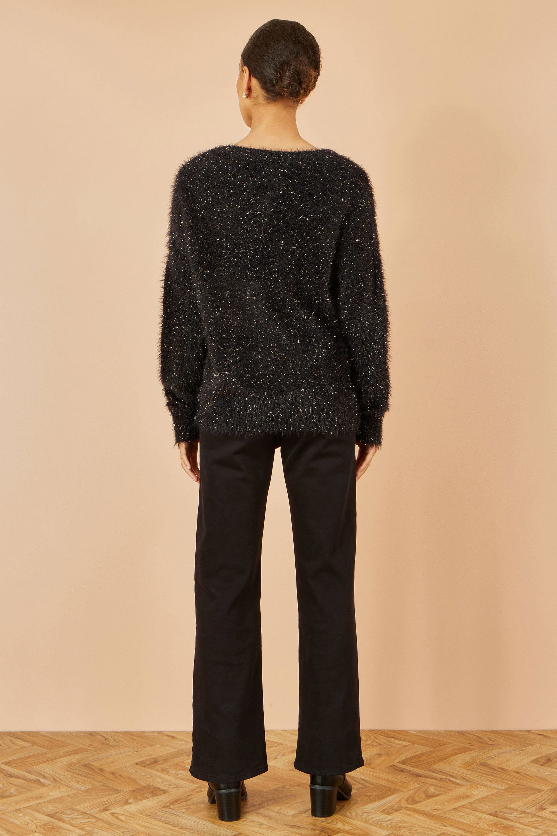 Person wearing a black textured sweater and pants against a beige wall.
