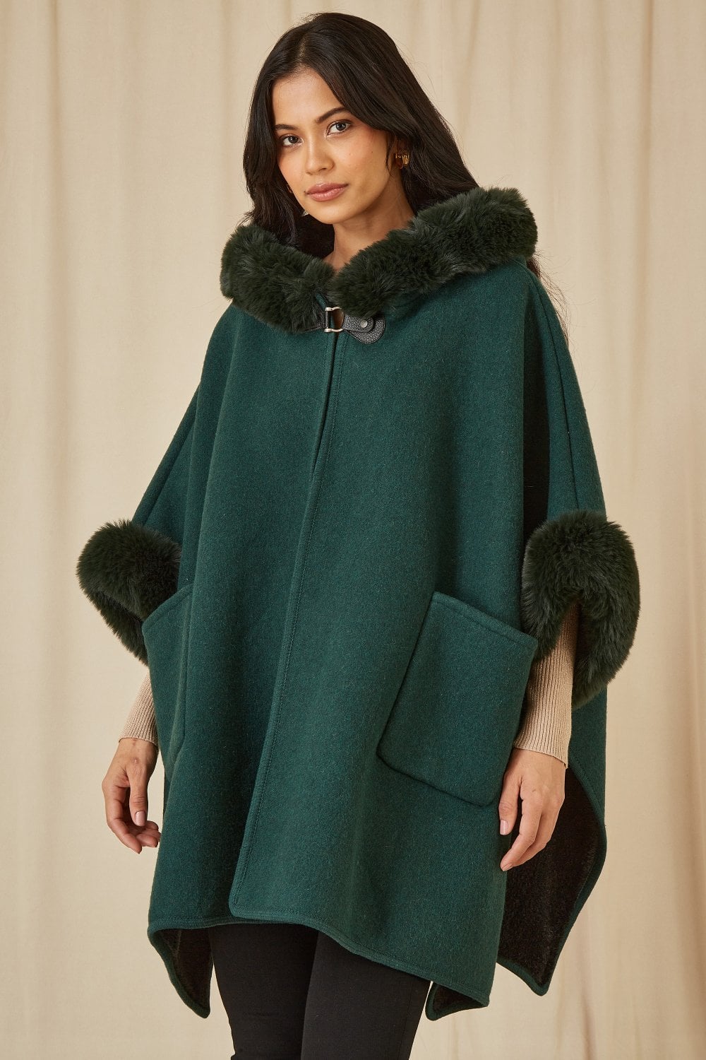 Woman wearing a teal poncho with black fur trim against a beige background
