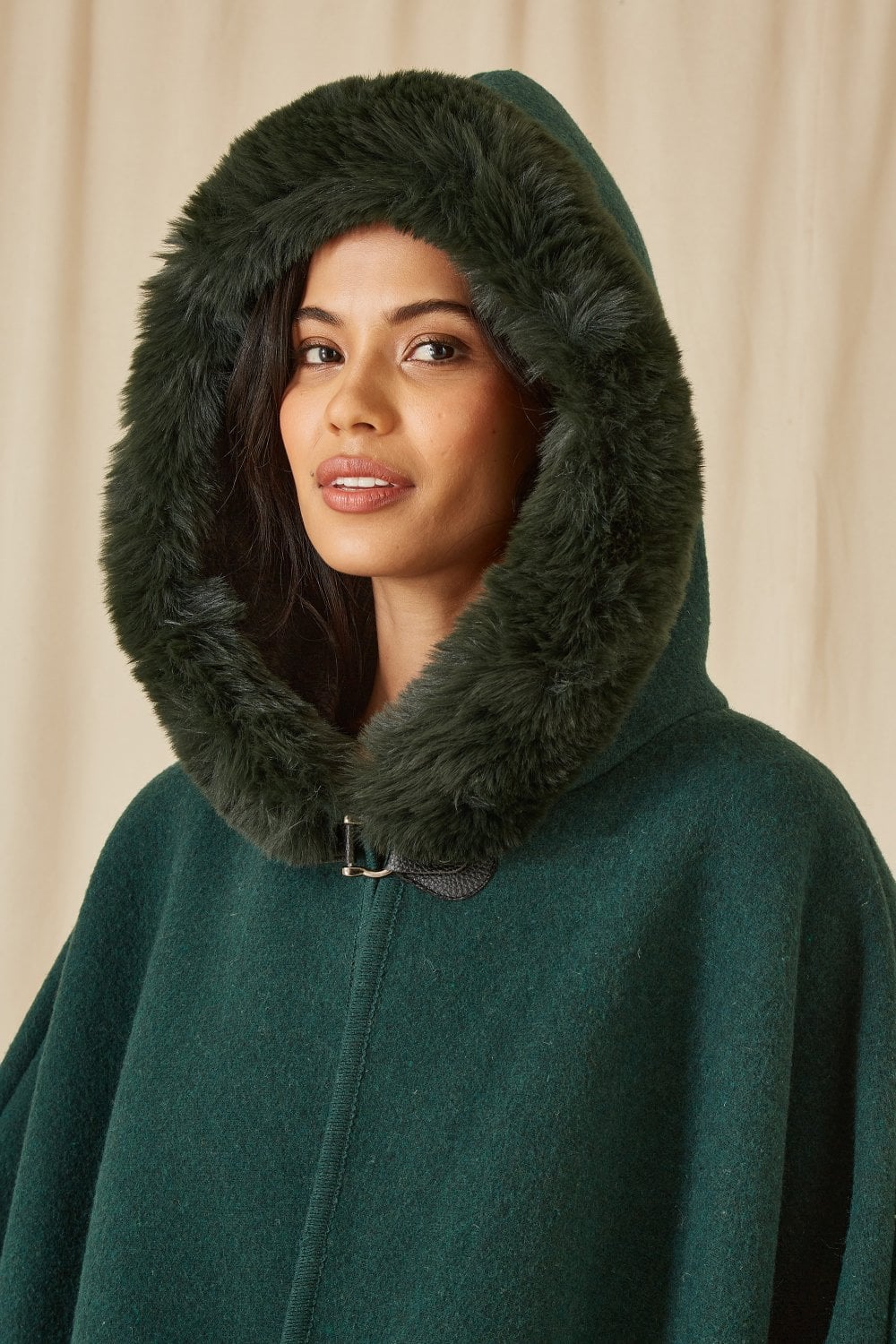 Woman wearing a green hooded coat with fur trim against a beige background